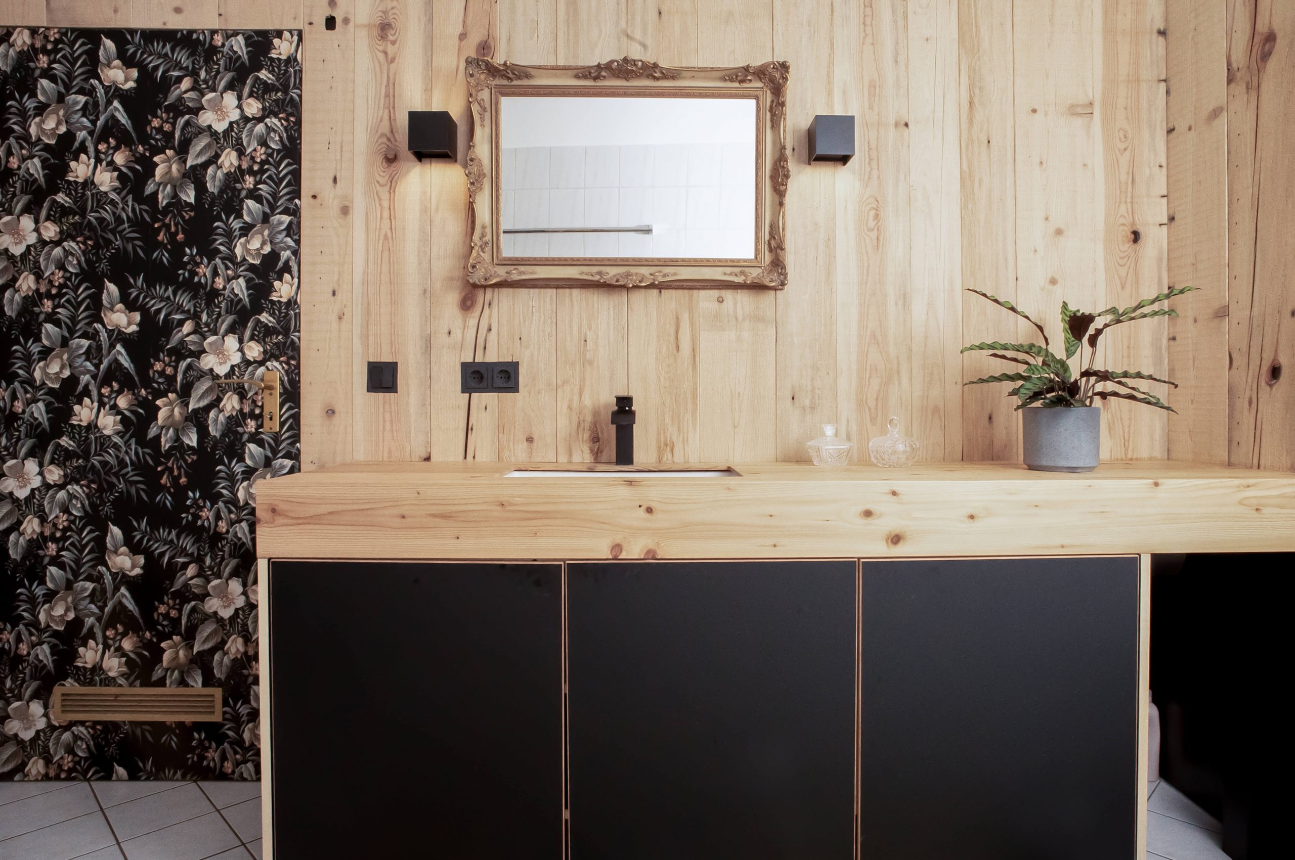 Studio F+ Interior Wandverkleidung aus Sägerauem Altholz kombiniert mit modernen Materialien wie ultramatten Fronten und kubischen Wandstrahlern, dazu ein historischer Spiegel.